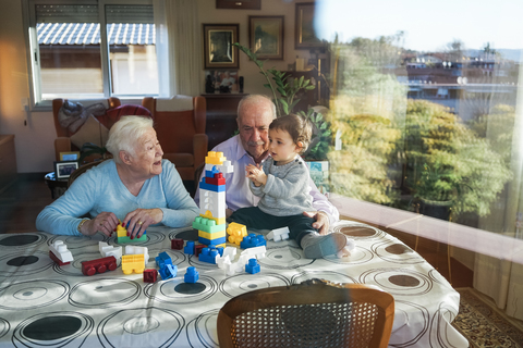 Great-grandparents and baby girl playing together with plastic building bricks at home stock photo