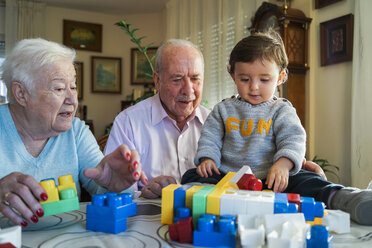 Urgroßeltern und kleines Mädchen spielen zusammen mit Plastikbausteinen zu Hause - GEMF01860