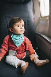 Baby sitting on a plane next to the window with a seat belt fasten - GEMF01865