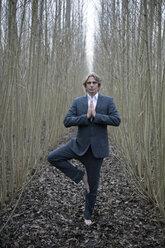 Businessman practicing yoga amidst willows - PSTF00067