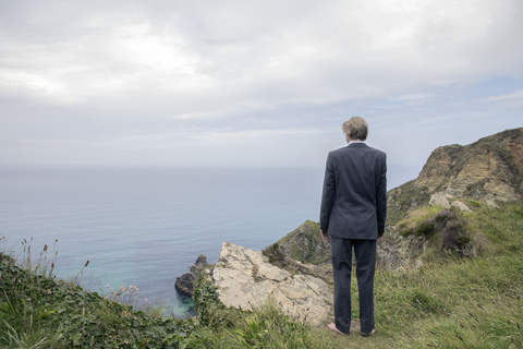 UK, Cornwall, Gwithian, Geschäftsmann steht an der Küste und betrachtet die Aussicht, lizenzfreies Stockfoto