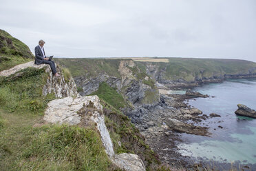 UK, Cornwall, Gwithian, Geschäftsmann an der Küste sitzend mit Laptop - PSTF00076