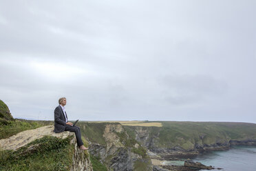 UK, Cornwall, Gwithian, Geschäftsmann an der Küste sitzend mit Laptop - PSTF00077