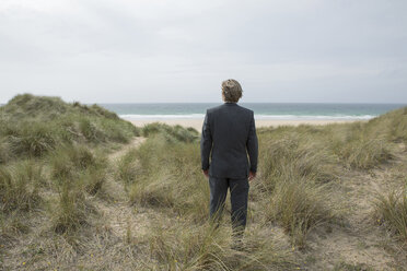 UK, Cornwall, Hayle, businessman standing in beach dunes looking at view - PSTF00078