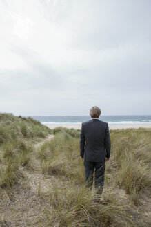 UK, Cornwall, Hayle, Geschäftsmann steht in den Stranddünen und betrachtet die Aussicht - PSTF00079