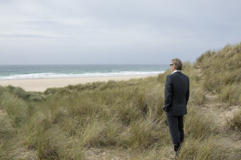 UK, Cornwall, Hayle, Geschäftsmann steht in den Stranddünen und betrachtet die Aussicht - PSTF00081