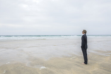 UK, Cornwall, Hayle, businessman standing on the beach looking at view - PSTF00082