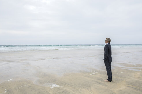 UK, Cornwall, Hayle, Geschäftsmann steht am Strand und betrachtet die Aussicht - PSTF00082