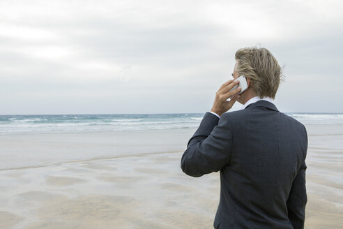 UK, Cornwall, Hayle, Geschäftsmann am Strand, der mit einem Handy telefoniert - PSTF00083