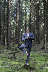 Businessman practicing yoga in forest - PSTF00089