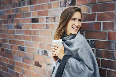 Porträt einer jungen Frau mit Kaffee zum Mitnehmen vor einer Backsteinmauer - BSZF00208
