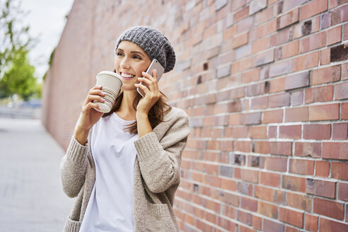 Portrait of happy woman with coffee to go on the phone - BSZF00222