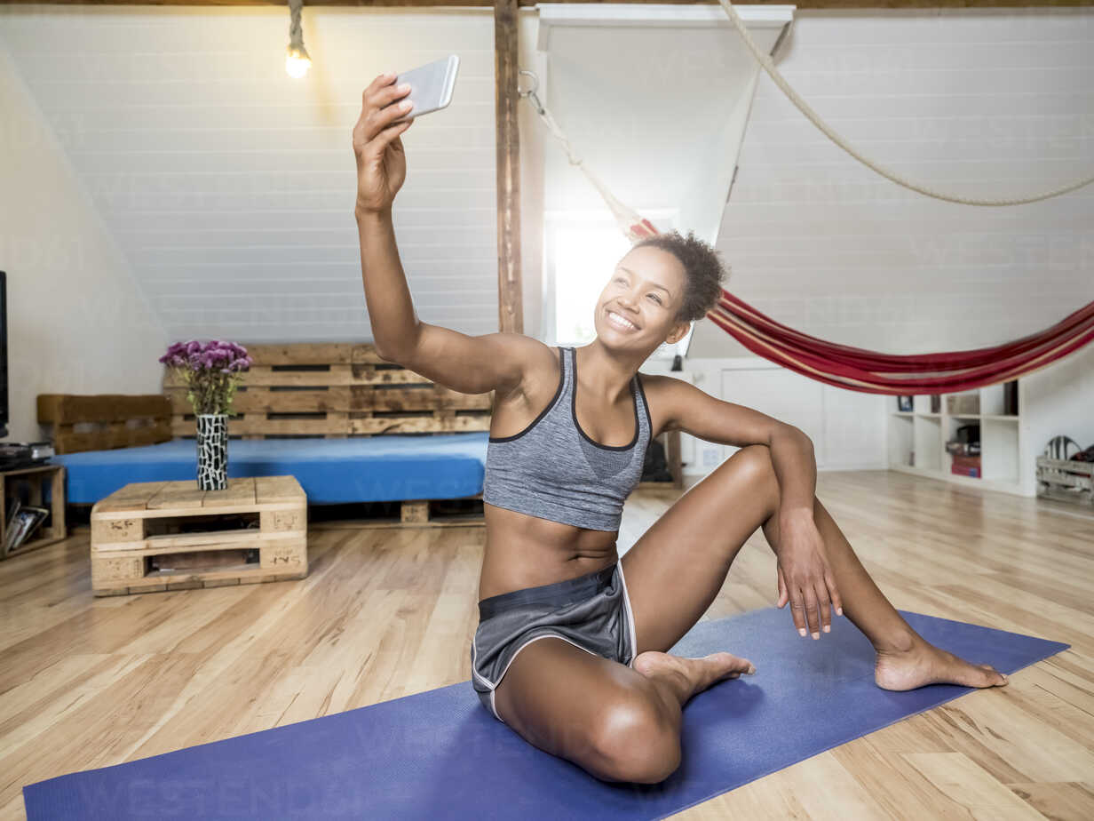 Smiling young woman sitting on yoga mat taking a selfie stock photo