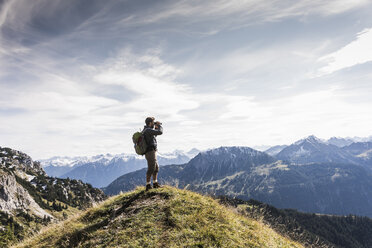 Österreich, Tirol, junger Mann steht in einer Berglandschaft und betrachtet die Aussicht mit einem Fernglas - UUF12573