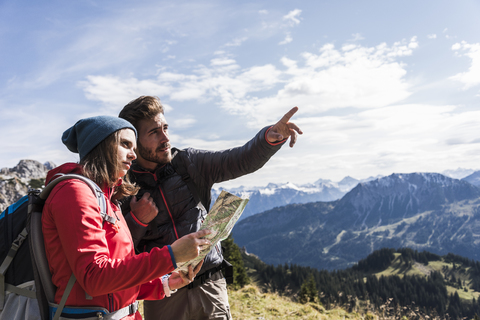 Österreich, Tirol, junges Paar mit Landkarte in Berglandschaft, das sich umschaut, lizenzfreies Stockfoto