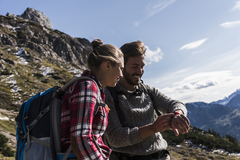 Österreich, Tirol, lächelndes junges Paar mit Blick auf die Uhr in einer Berglandschaft, lizenzfreies Stockfoto