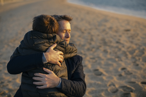 Vater, der seinen Sohn am Strand umarmt, lizenzfreies Stockfoto