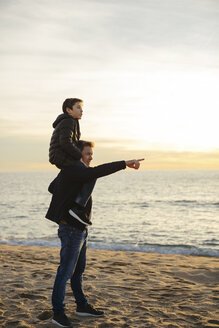 Vater trägt Sohn huckepack am Strand bei Sonnenuntergang und zeigt mit dem Finger - EBSF02032