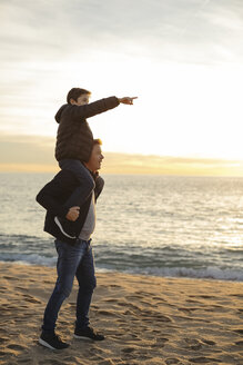 Vater trägt Sohn huckepack am Strand bei Sonnenuntergang und zeigt mit dem Finger - EBSF02033