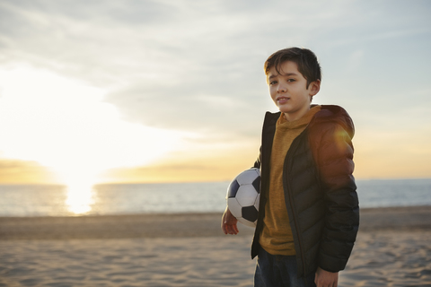 Portrait of boy holding football on the beach at sunset stock photo