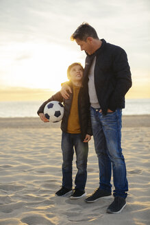 Vater umarmt Sohn mit Fußball am Strand bei Sonnenuntergang - EBSF02038