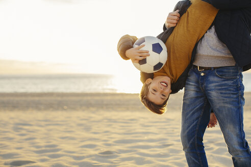 Vater hält Sohn mit Fußball kopfüber am Strand bei Sonnenuntergang - EBSF02045