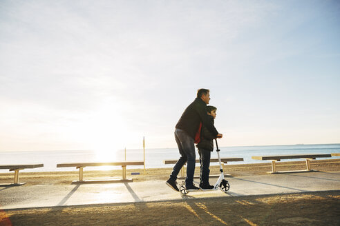Vater und Sohn fahren Roller auf der Strandpromenade bei Sonnenuntergang - EBSF02046