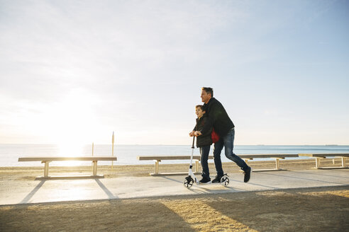 Vater und Sohn fahren Roller auf der Strandpromenade bei Sonnenuntergang - EBSF02047