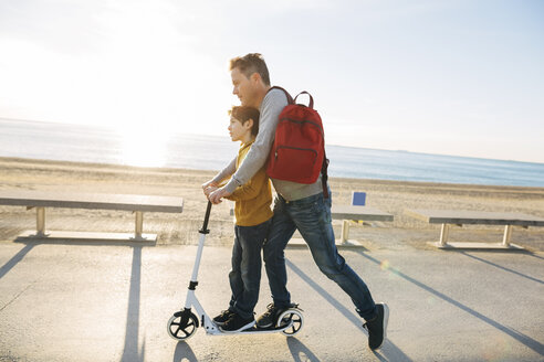 Vater und Sohn fahren Roller auf der Strandpromenade bei Sonnenuntergang - EBSF02052
