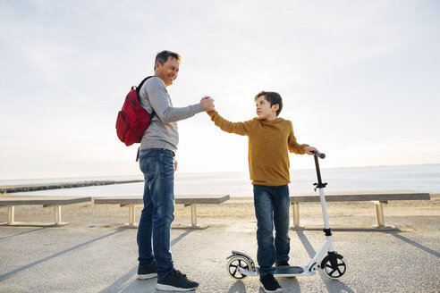 Vater und Sohn mit Motorroller schütteln sich auf der Strandpromenade bei Sonnenuntergang die Hände - EBSF02054