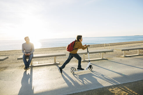 Vater beobachtet Sohn beim Rollerfahren auf der Strandpromenade bei Sonnenuntergang - EBSF02056