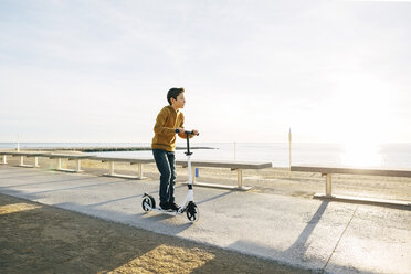Junge fährt Roller auf der Strandpromenade bei Sonnenuntergang - EBSF02059