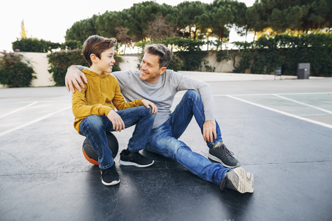 Vater umarmt Sohn auf Basketballplatz im Freien, lizenzfreies Stockfoto