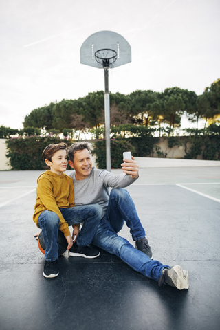 Vater und Sohn sitzen auf einem Basketballplatz im Freien und machen ein Selfie, lizenzfreies Stockfoto