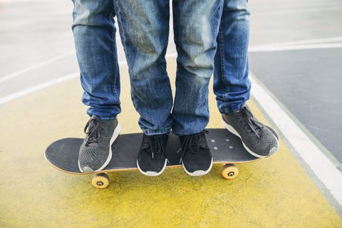 Beine eines Erwachsenen und eines Kindes auf einem Skateboard, lizenzfreies Stockfoto