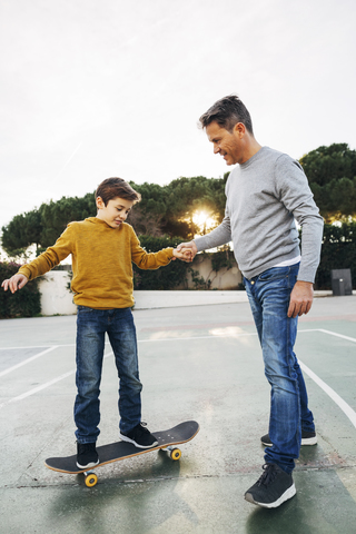 Vater hilft seinem Sohn beim Skateboardfahren, lizenzfreies Stockfoto