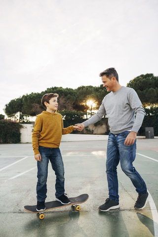 Father assisting son riding skateboard stock photo