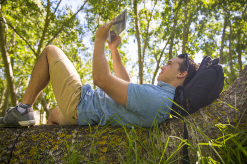 Mann liegend auf Baumstamm in der Natur nimmt Selfie mit Tablet - ZEF14943