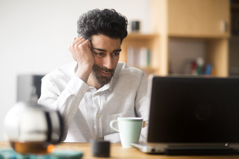 Portrait of businessman at desk looking at laptop - SGF02156