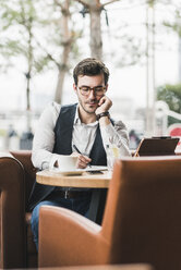 Young man working in a cafe using tablet and taking notes - UUF12599