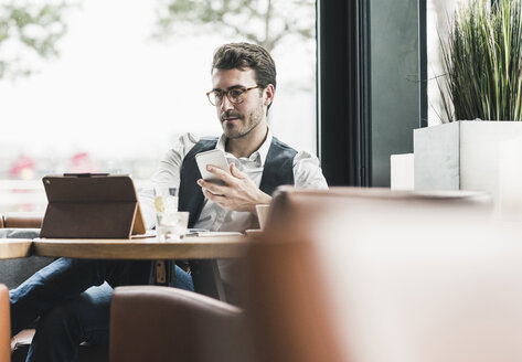Junger Mann arbeitet in einem Café mit Tablet und Mobiltelefon - UUF12603