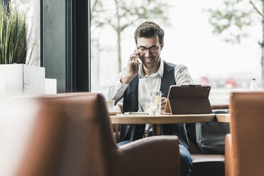 Smiling young man working in a cafe talking on cell phone - UUF12604