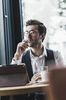 Junger Mann arbeitet in einem Café mit Tablet und macht sich Notizen - UUF12607