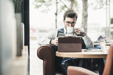 Young man working in a cafe using tablet and drinking coffee - UUF12608