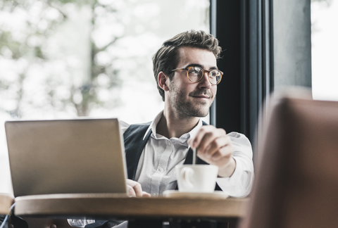 Smiling young man in a cafe with laptop and cup of coffee stock photo