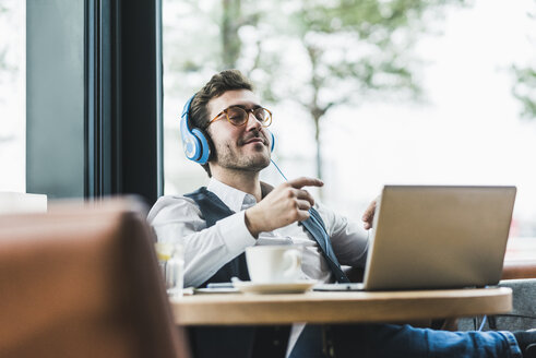 Junger Mann in einem Café mit Laptop und Kopfhörern beim Entspannen - UUF12616
