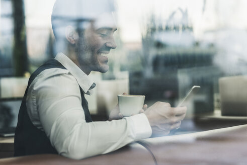 Lächelnder junger Mann in einem Café, der auf sein Handy schaut - UUF12621