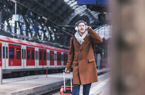 Junger Mann mit Gitarrenkoffer und Kopfhörern auf dem Bahnsteig - UUF12622