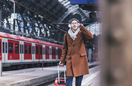 Young man with guitar case and headphones at station platform - UUF12622