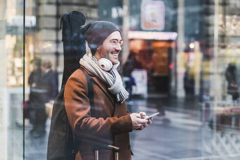 Smiling young man with guitar case and cell phone - UUF12624